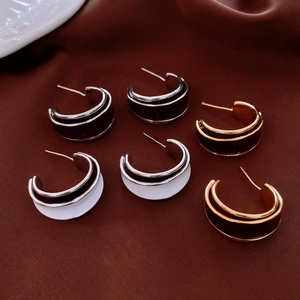 Detailed macro of C-shaped enamel hoop earrings on brown silk fabric background