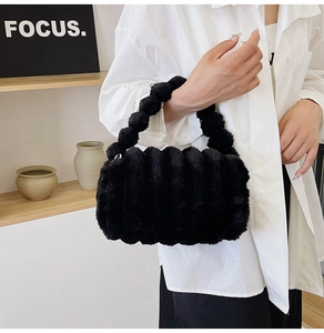Detail of black faux fur handbag with unique plush ball handle shown in hand