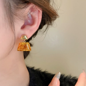 Close-up of trapezoidal amber resin earrings with gold metallic texture on model