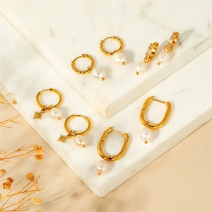 Detailed arrangement of gold U-shaped and geometric pearl earrings on marble surface