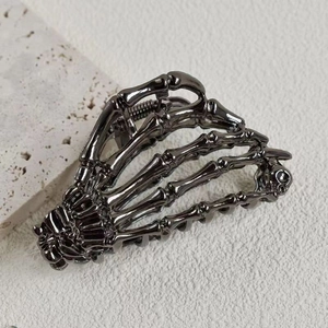 Detail view of a dark gunmetal skeleton hand hair claw clip on a textured stone surface