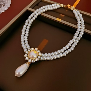 Close-up of double-layer pearl necklace with a gold flower charm and teardrop pearl pendant
