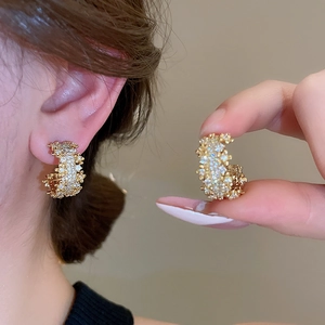 Macro detail of C-shaped golden earrings with micro-paved zircons and silver needle studs