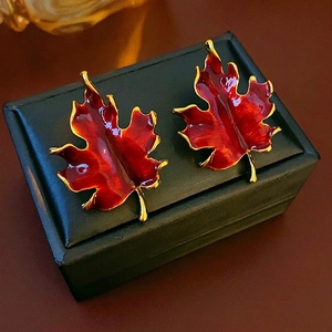 Vintage maple leaf earrings with red enamel and gold trim on a black leather jewelry box