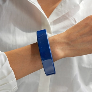 Détail d'un bracelet large en résine bleu foncé brillant porté sur une manche de chemise