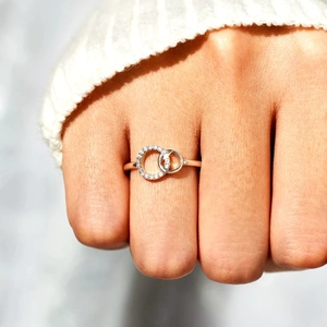 Intertwined rose gold rings with pavé crystals on a hand with white knitted cuff