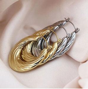 Detailed view of twisted teardrop hoop earrings in gold and silver on silk fabric