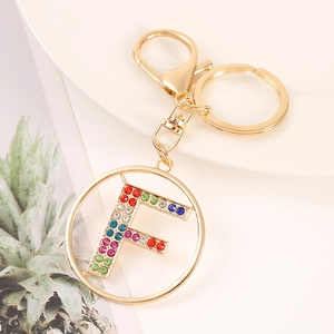 Detail of a gold-plated letter F keychain with colorful rhinestones on white ceramic