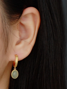 Close-up of a gold-plated C-shaped earring featuring a round green aventurine gemstone pendant