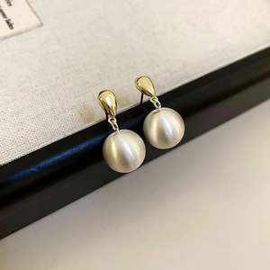 Détail de boucles d'oreilles dorées avec grandes perles blanches mates en goutte