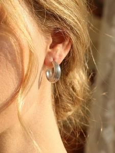 Gros plan d'une boucle d'oreille argentée en forme de C avec rayures verticales