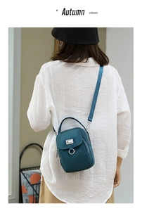 Detail of peacock blue nylon crossbody bag with multi-layer zippers on white shirt