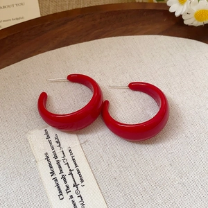 Détail de boucles d'oreilles en résine rouge en forme de C sur fond de lin et décor floral