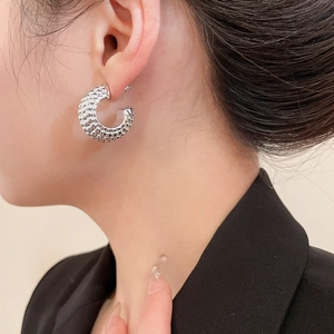 Close-up of silver C-shaped earrings with textured surface on a female model