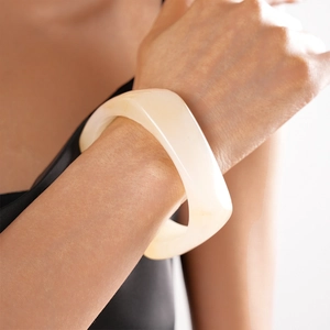 Close-up of wide irregular cream resin bangle featuring a smooth geometric minimalist finish