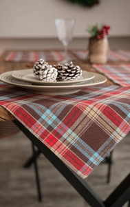 Detailed view of festive red and brown plaid table runner on a wooden dining table