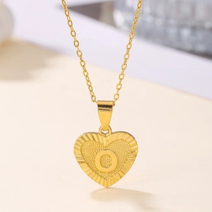 Detail of a gold heart pendant necklace featuring an engraved letter O with textured finish