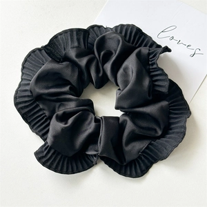 Detailed view of the pleated black satin hair scrunchie with ruffled edges and silky texture