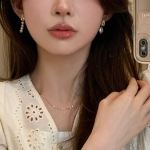 Detail of elegant baroque pearl earrings and thin gold necklace worn by a female model
