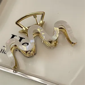 Close-up of golden wavy hair claw clip with white mica inlay on a beige display card