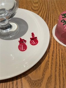 Detailed close-up of red Fu character earrings with bowknot on a white ceramic plate