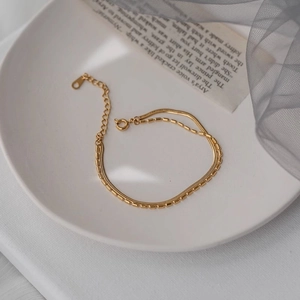 Elegant gold double-layered snake chain bracelet displayed on a white ceramic plate
