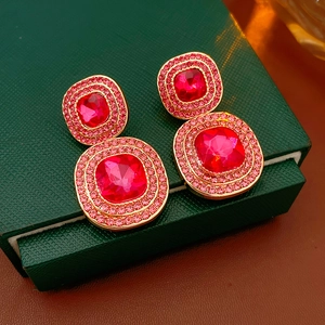 Close-up of vintage gold earrings with layered red square gemstones and pink crystals
