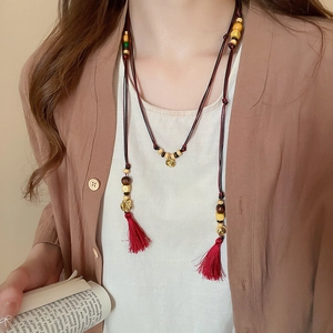 Detailed shot of ethnic long necklace with wooden beads, red tassels and golden charms