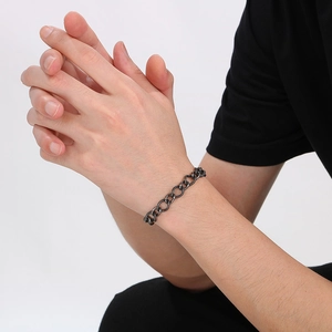 Detailed view of dark grey stainless steel curb chain bracelet worn on a model's wrist