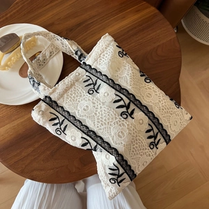 Detail of vintage lace tote bag with black floral embroidery on a wooden table
