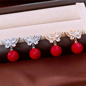 Detailed macro view of zircon butterfly earrings with festive red bead drops in a jewelry box