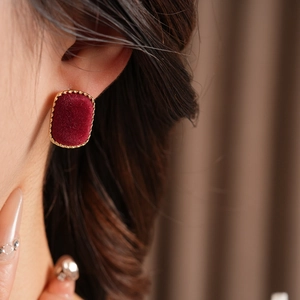 Detail of red velvet square earring with twisted gold metal frame worn by a model