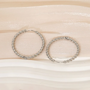 Pair of minimalist silver twist hoop earrings in stainless steel on white pedestal