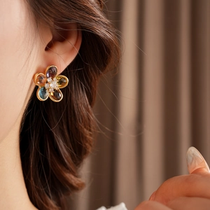 Close-up of elegant flower earrings with multicolor zircons and gold setting on model