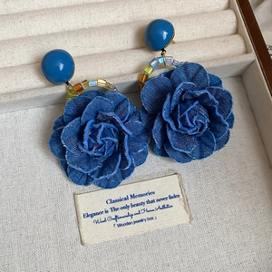 Détail des boucles d'oreilles rose en denim bleu avec perles sur fond texturé blanc