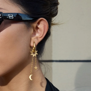 Détail de boucles d'oreilles pendantes en acier doré avec pampilles étoile et lune