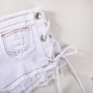 Dettaglio di pantaloncini in denim bianco con lacci laterali, cuciture arancioni e orli sfrangiati