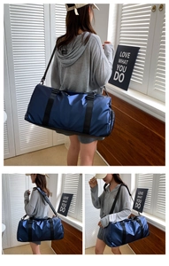 Deep blue cylindrical fitness travel bag with black handles and shoulder strap shown in room
