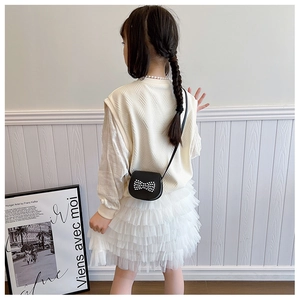Rear view of girl in cream knit vest and white tutu skirt with small black pearl handbag