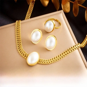 Detailed set of gold-plated oval pearl necklace, open ring, and stud earrings on velvet
