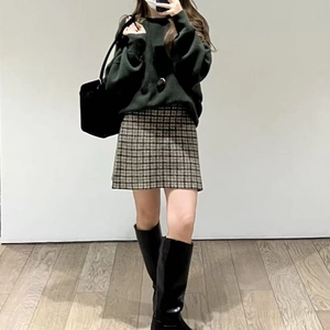 Dettaglio di un maglione verde scuro abbinato a una gonna scozzese e stivali alti in pelle neri