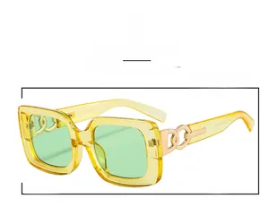 Detail view of square amber sunglasses featuring gold metal chain links and green lenses