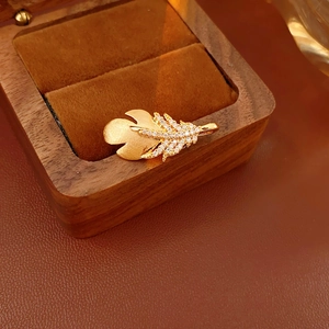 Detail of a gold feather brooch with zircon stones on a dark wood jewelry box