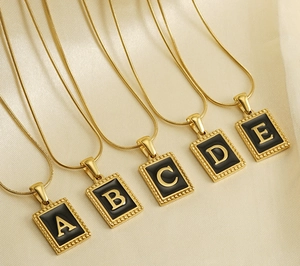 Detail view of 18K gold titanium square letter pendants on sleek snake chains