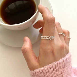 Close-up of a silver chain link ring worn by a model in a cozy lifestyle setting