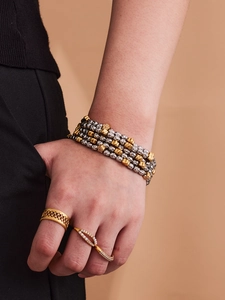 Detailed close-up of layered beaded bracelet and hollow grid gold ring on model hand