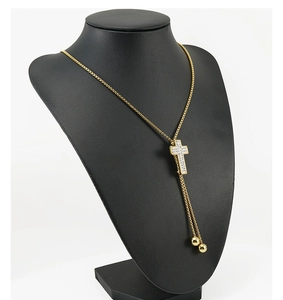 Detail of 18K gold-plated cross necklace with white rhinestones and golden beads on a mannequin