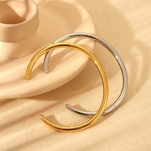 Polished 18K gold and silver stainless steel cuff bracelets on a ceramic tray