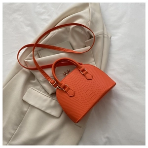 Detail shot of bright orange shell bag with crocodile texture and gold hardware details