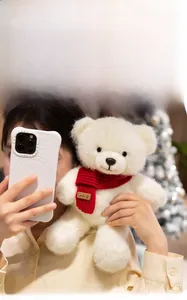 Close-up of a white plush teddy bear wearing a red knit scarf with a smile label